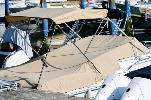 Partial shot close up of beige foldable roof sun shade bikini bimini top sun sail sun canopy and sport boat motor boat covered with brown canvas in a harbor as a concept for protection from sun wind and weather