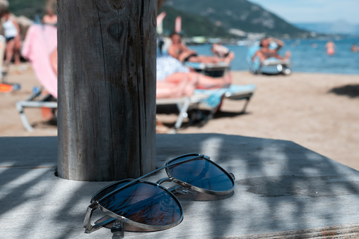 Sunglasses in the foreground, out of focus beach and tourists sunbathing in the background.