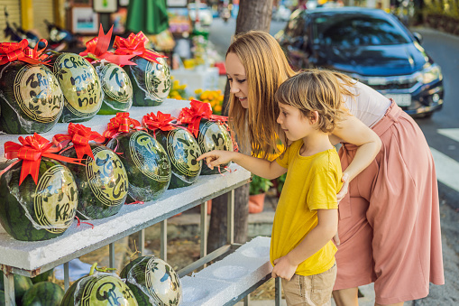 Mom and son tourists look at Watermelons with festive engraving on Tet Eve. Tet is Lunar New Year and celebrated during four days in Vietnam.