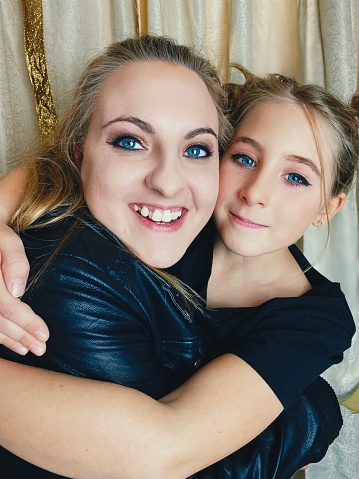 Mother and daughter time at a Homemade Photo Booth Party. The two have their faces up against each other, looking very alike and taking a portrait at home during a birthday party. They are looking at the camera, both blue-eyed and beautiful.