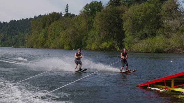 Two water skiers go off jump, slow motion