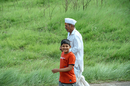 Pune, India - July 23 2023: Portrait of a young Indian kid walking with an elderly man at a village near Pune India.