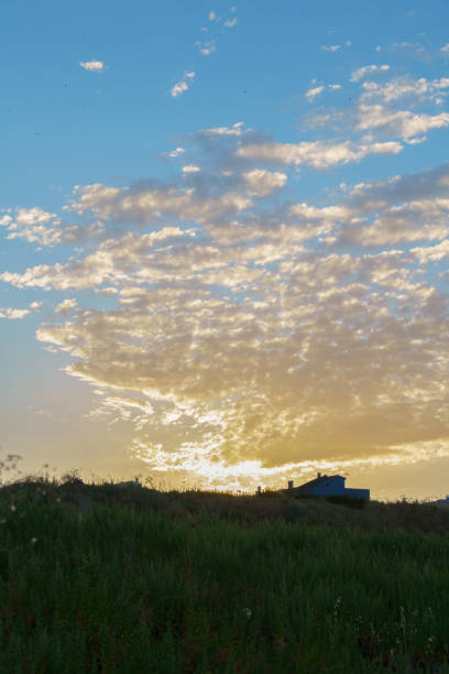 colorful sunrise with clouds with a meadow and a house in the background , lights and shadows
