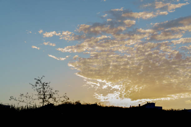 colorful sunrise with clouds with a meadow and a house in the background , lights and shadows
