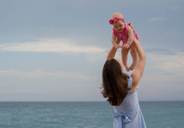 Young beautiful mother playing with her baby on the beach
