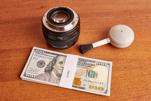 Bundle of dollars with hobby inscription, lens and cleaning brush. Hobby money concept.