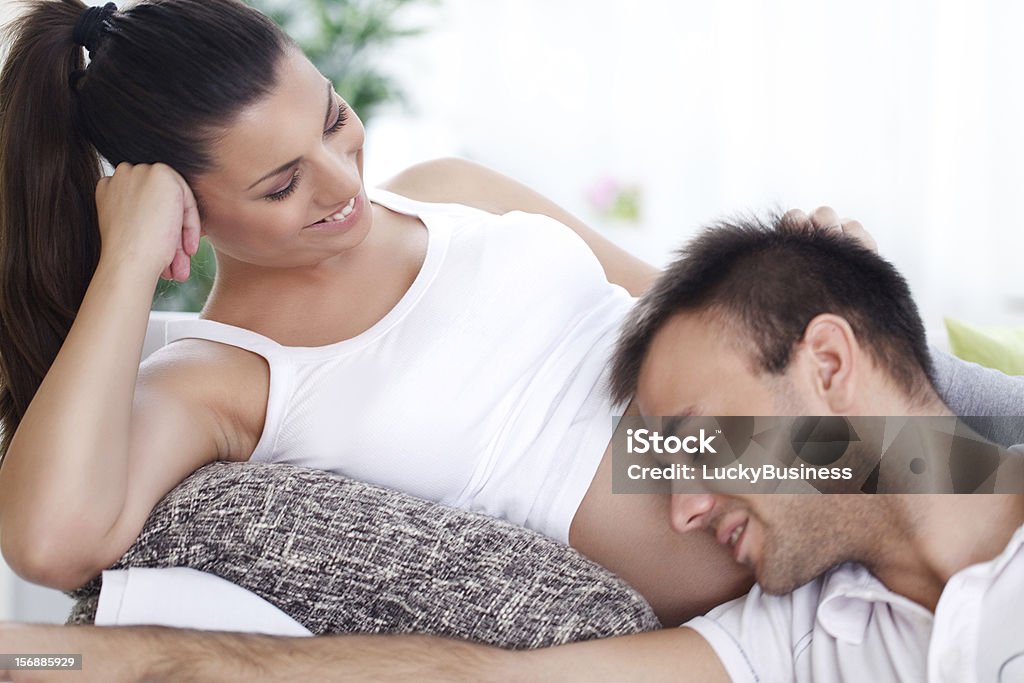 Husband listening to his wife's belly Happy future dad listening the belly of his pregnant wife Abdomen Stock Photo