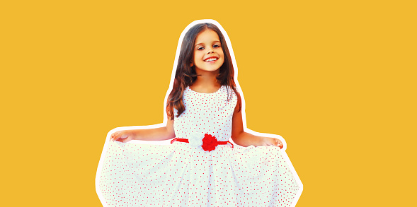 Portrait of cheerful smiling little girl child having fun wearing white dress on yellow background