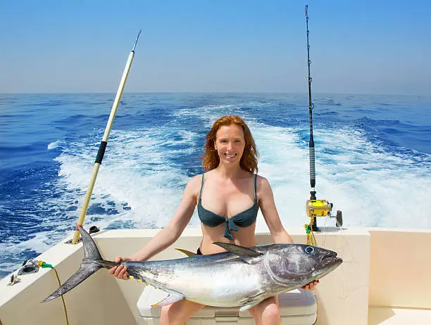 Photo of bikini fisher woman holding bluefin tuna on boat