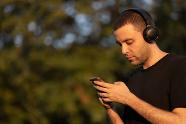 Young man is texting a message on smart phone at public park.