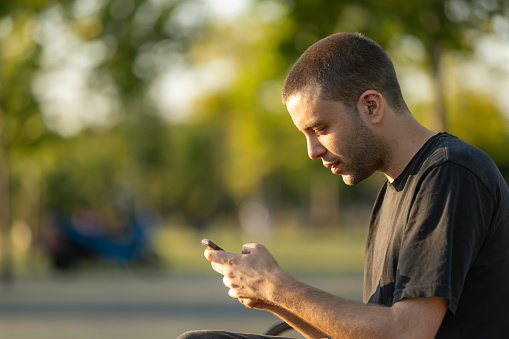 Portrait of young man. He is texting a message on smart phone on the outside.