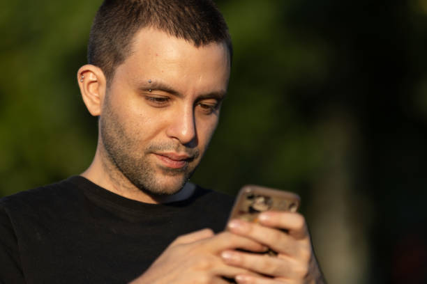 istock Young handsome man is typing a message on mobile phone at public park. 1568890705