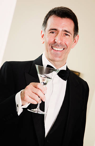 homem maduro no smoking levanta copo de martini a sorrir - high society men tuxedo party imagens e fotografias de stock