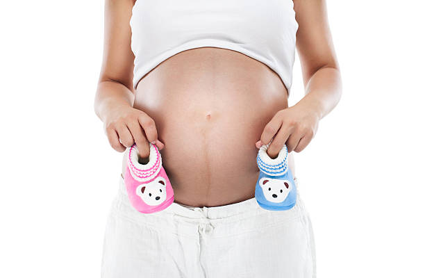 pregnant woman holding baby booties, pink for a girl and blue for a boy.