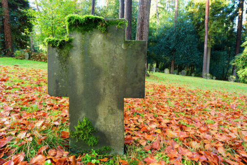Grave headstone of a German soldier in fall. Tombstone covered with moss and autumn leaves. German war graves in the the forest cemetery, Aachen, Germany.