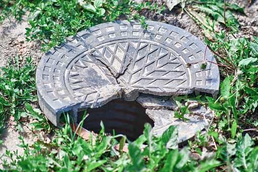 A broken metal manhole cover, an open well in the grass