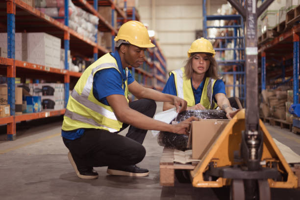 istock Warehouse workers inspect goods together on pallet trucks in a large warehouse 1568915615