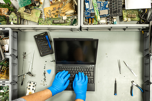 Overhead view of man's hands repairing laptop in recycling centre.