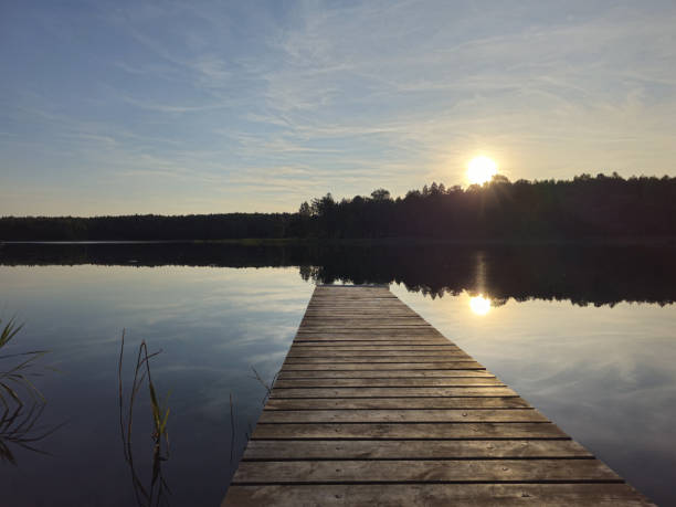 istock Wooden bridge to a calm lake. Setting sun. 1568929692