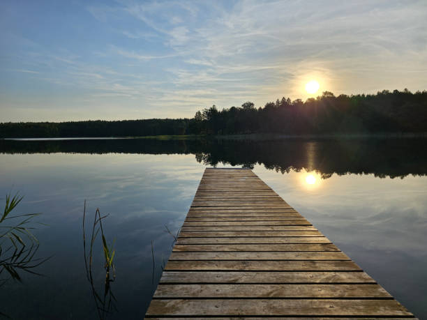 istock Wooden bridge to a calm lake. Setting sun. 1568931287