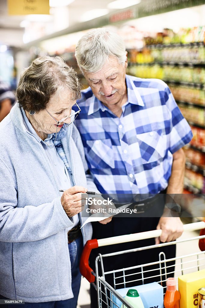 Senior shoppers check grocery list in supermarket A senior couple check their list while shopping together for groceries in the supemarket. The labels on the products in the cart are made by the photographer.  80-89 Years Stock Photo