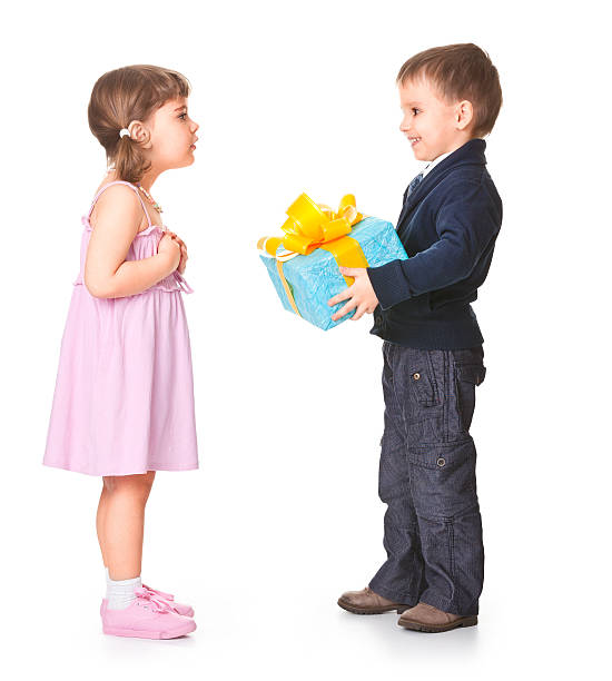 African American children sit together in a yard, picking and examining flowers.  Cute brother and sister interactions.