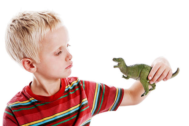 istock Cute 6 year old blond boy examines toy dinosaur 156894108