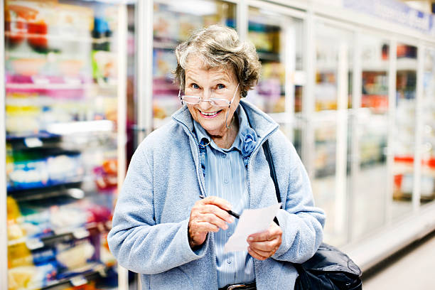 senior donna al supermercato controlli lista della spesa, sorride delightedly - senior adult aging process supermarket shopping foto e immagini stock