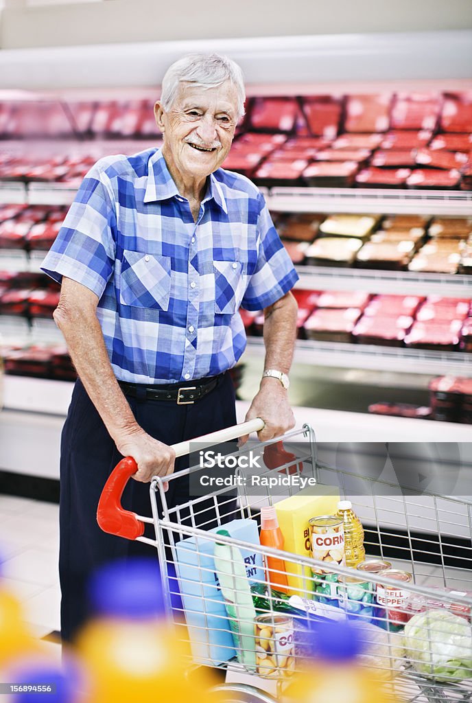 Souriant homme senior pousse tramway devant un supermarché viande réfrigérateur - Photo de Activité libre de droits