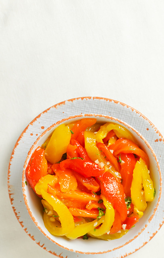 Sliced red and yellow roasted peppers in a white ceramic bowl. Concept of healthy eating. Traditional Italian dish. Vegetarian and vegan food. Vertical orientation. Top view. Copy space