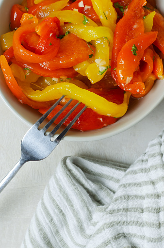 Salad with red and yellow roasted pepper slices, garlic and parsley in a gray ceramic bowl with a fork. Concept of healthy eating. Traditional Italian dish. Horizontal orientation. Top view