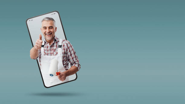 istock Confident painter and decorator  in a smartphone videocall and smiling, online  service concept 1568959370