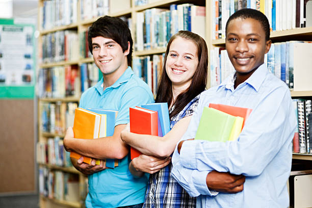 istock Three happy students in library with arms full of books 156896923