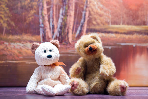 Small  Brown and Beige Teddy bear sitting on a bench with an autumn scene in the back ground.
