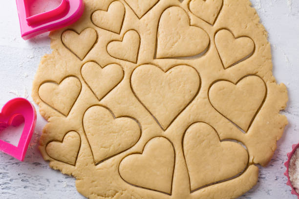 istock Cutting heart shaped cookies with cookie cutters on a light blue tabletop, top view. Stage of cooking delicious homemade pastry 1569014823