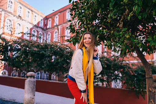 girl in stylish clothes posing near a tree on the background of a building with a red facade. Lisbon, Portugal.