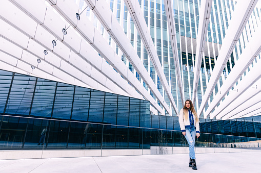 Beautiful young girl thoughtfully stands on the street against the background of a glass office building