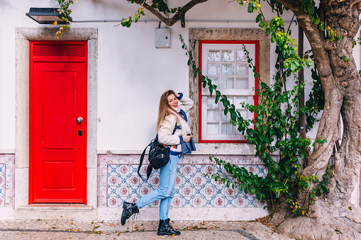 stylish girl posing near a building with white walls and red doors. beautiful facade of a building on the street of Lisbon.