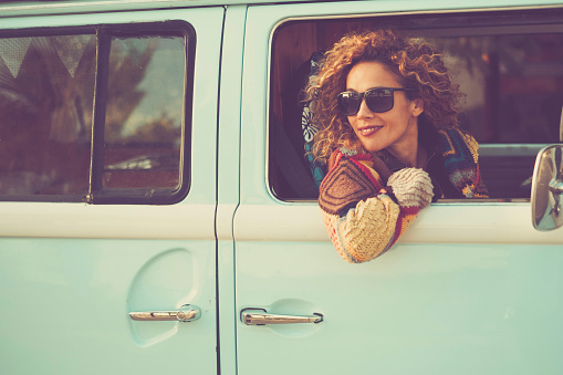 Retro classic travel vehicle and people concept. One Beautiful adult woman inside a blue van. Transport vehicle and freedom. Alternative lifestyle lady sith curly hair. Cheerful female traveler smile