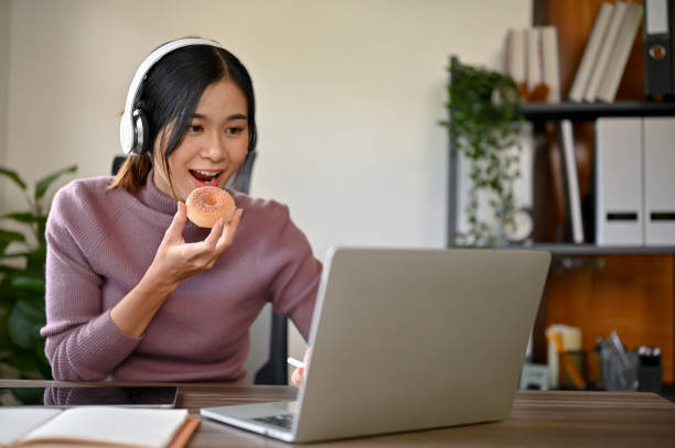 Beautiful young Asian girl eating a donut while studying at her study table