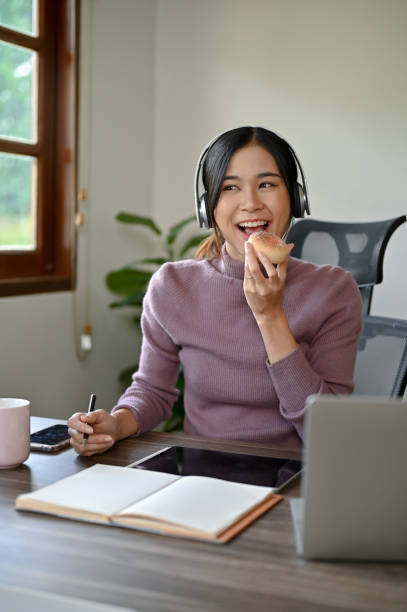 Beautiful Asian girl eating a donut while studying at her study table in her house