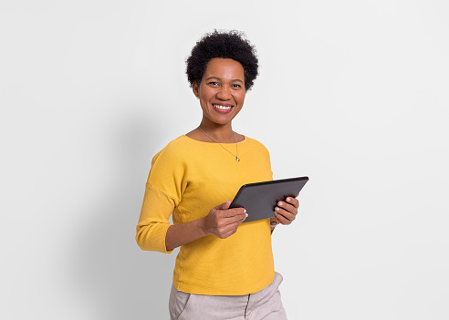 Portrait of smiling young businesswoman holding digital tablet and standing over white background
