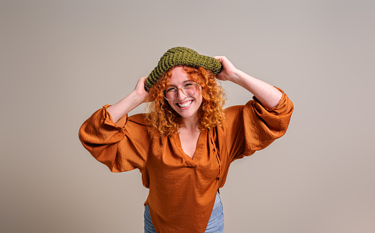 Portrait of smiling beautiful young woman wearing knit hat and posing cheerfully on background