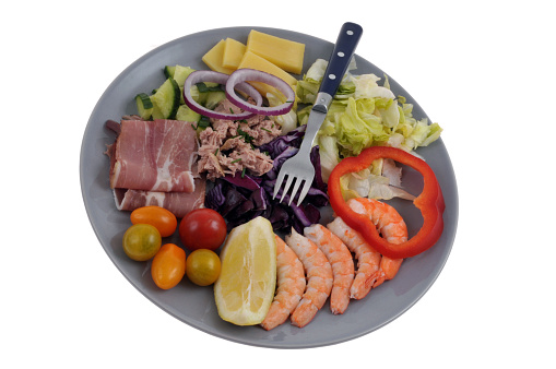 Mixed salad served in a plate with vegetables, raw ham and prawns close-up on a white background