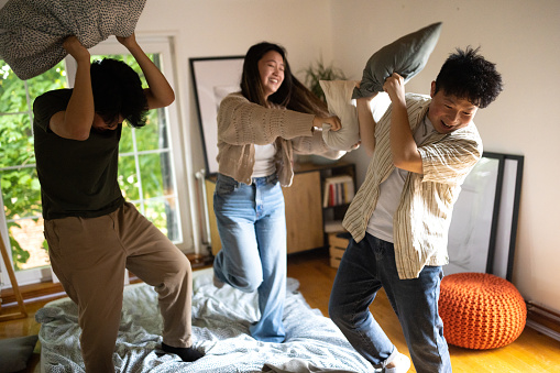 Group of young Chinese friends having a pillow fight in the bedroom of a house
