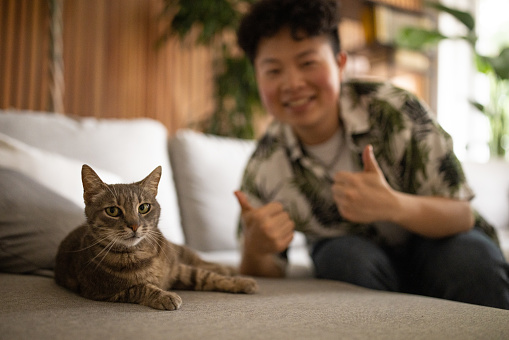 Young Chinese man posing for a picture with a cat in the living room of a house