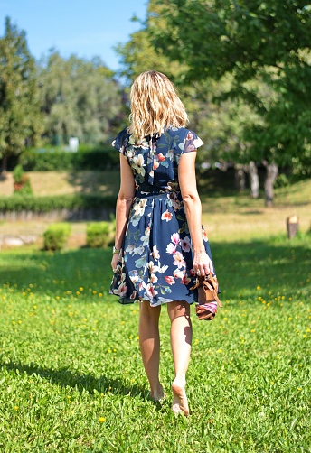 Beautiful blond woman in the park holding her shoes in hand