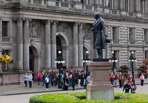 Glasgow, Scotland, UK - 23rd July 2023: Group of tourists and pedestrians outside Glasgow City Chambers in George Square in the city centre. The statue of James Oswald, former Glasgow MP, by Baron Marochetti, is in the foreground.