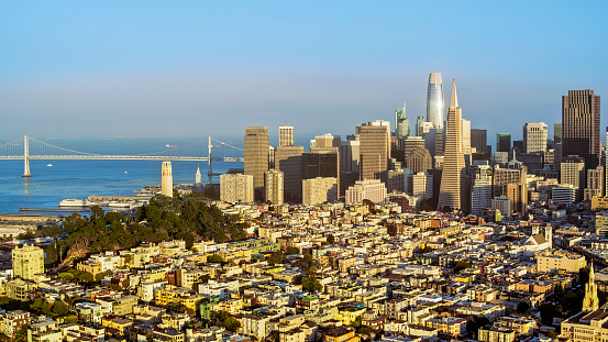 Aerial view of skyscraper buildings in city and Oakland Bay Bridge during sunset, San Francisco, California, USA.