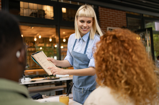 Happy waitress assisting her customers in choosing a dish from a Menu at restaurant.